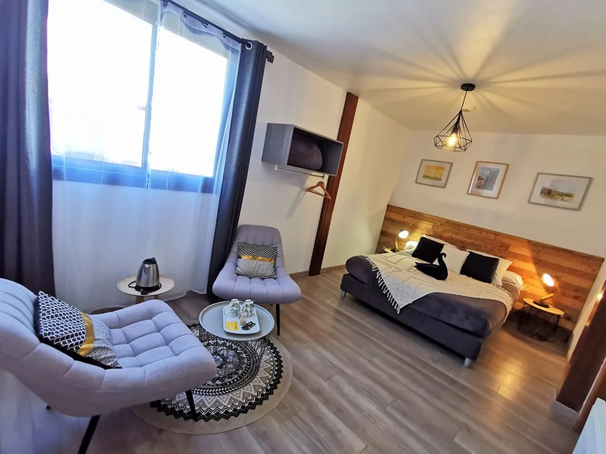 La chambre double confort, son lit à tête de lit en bois et son fauteuil